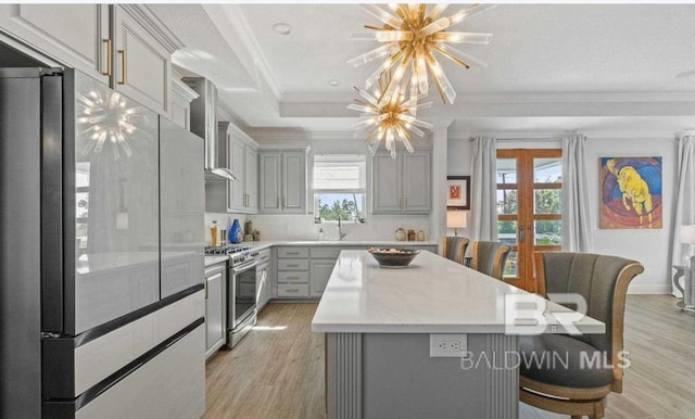 kitchen with stainless steel gas range oven, a raised ceiling, ornamental molding, gray cabinetry, and refrigerator with glass door