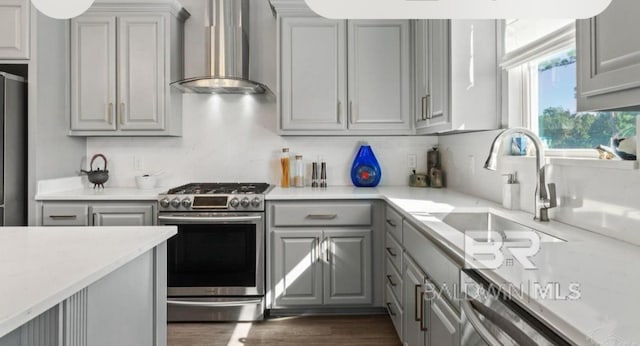 kitchen featuring dark wood-style floors, stainless steel appliances, gray cabinetry, a sink, and wall chimney exhaust hood