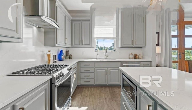 kitchen featuring stainless steel appliances, wall chimney exhaust hood, a sink, and gray cabinetry