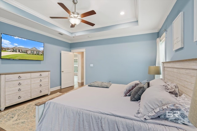 bedroom featuring baseboards, a raised ceiling, wood finished floors, and ornamental molding