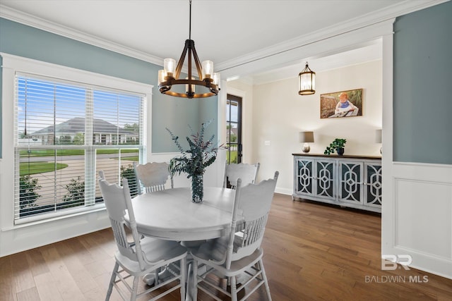 dining area with an inviting chandelier, crown molding, dark wood-type flooring, and wainscoting