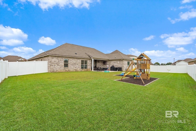 rear view of property featuring a playground, a lawn, brick siding, and a fenced backyard