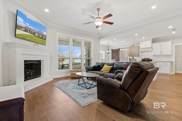 living area featuring a barn door, light wood-style flooring, and crown molding