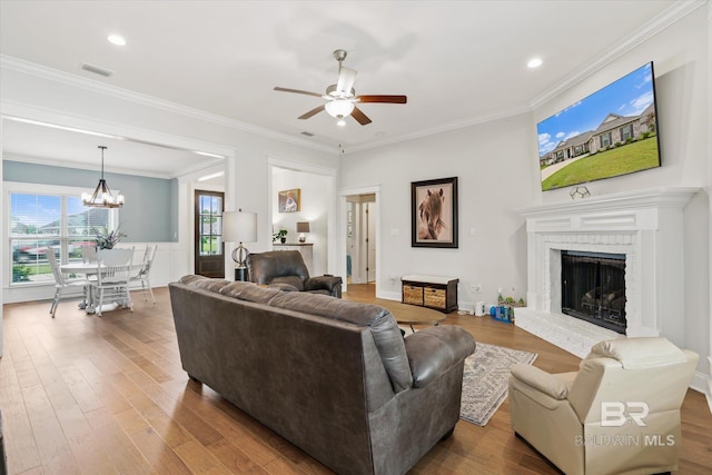 living area with visible vents, crown molding, ceiling fan with notable chandelier, a fireplace, and wood finished floors