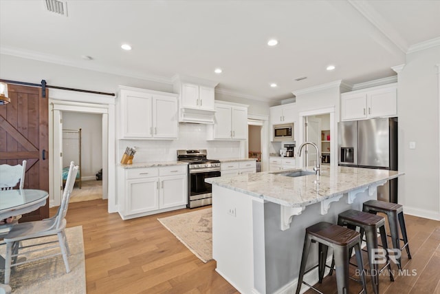 kitchen with visible vents, light wood-type flooring, a barn door, appliances with stainless steel finishes, and a sink