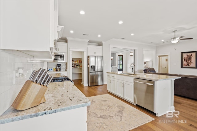 kitchen featuring a sink, open floor plan, white cabinetry, appliances with stainless steel finishes, and decorative backsplash