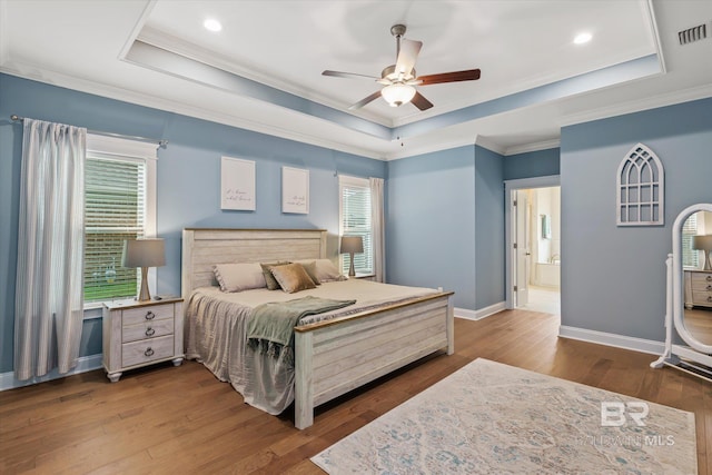 bedroom with visible vents, a tray ceiling, wood finished floors, crown molding, and baseboards