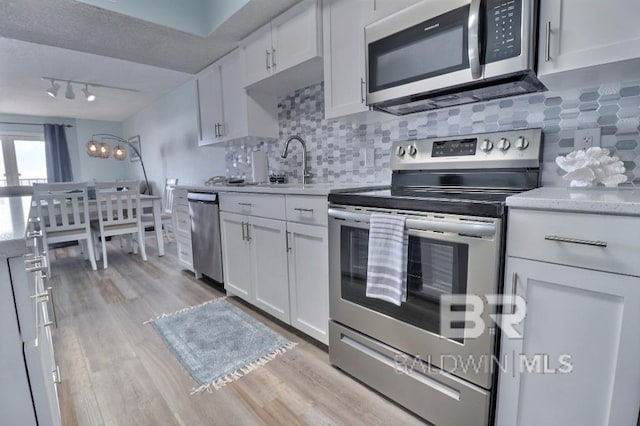 kitchen with appliances with stainless steel finishes, backsplash, sink, light hardwood / wood-style floors, and white cabinetry