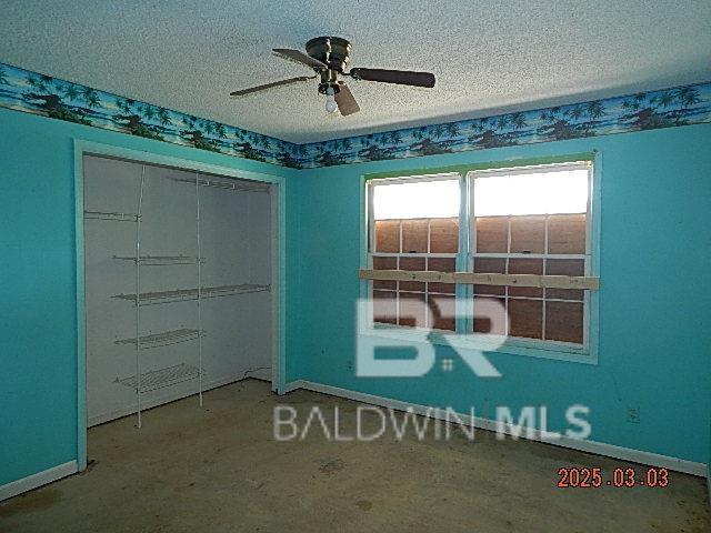 unfurnished room with a textured ceiling, ceiling fan, and baseboards