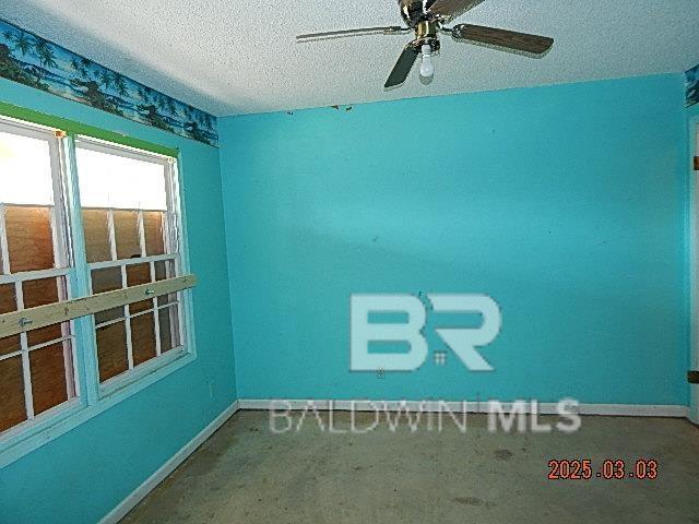 unfurnished room with a textured ceiling, ceiling fan, and baseboards