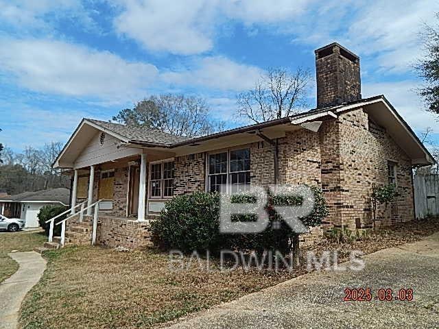 ranch-style house featuring a porch, brick siding, and a chimney