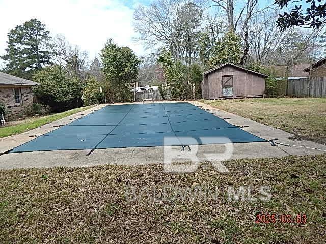 view of pool featuring an outbuilding, fence, a yard, a covered pool, and a patio area