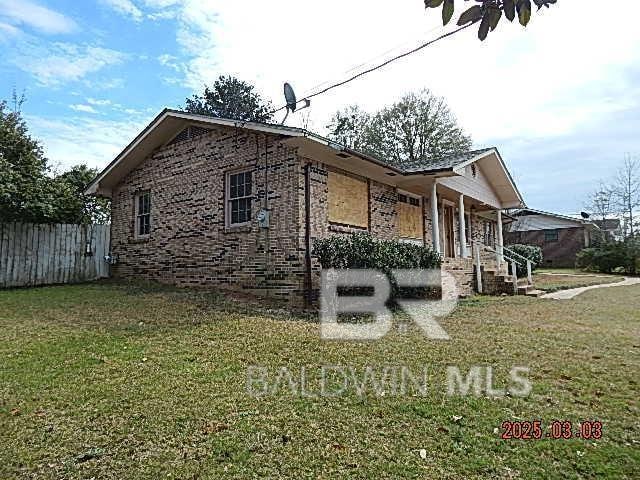 view of home's exterior with covered porch, fence, a lawn, and brick siding