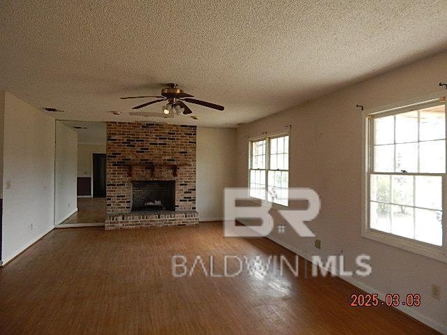 unfurnished living room featuring a brick fireplace, ceiling fan, a textured ceiling, and wood finished floors