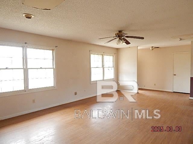 spare room with ceiling fan, a textured ceiling, baseboards, and wood finished floors