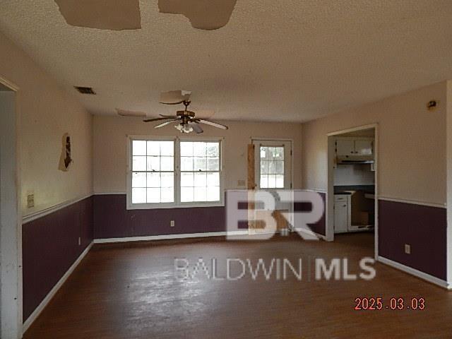 interior space featuring a wainscoted wall, visible vents, a ceiling fan, a textured ceiling, and wood finished floors