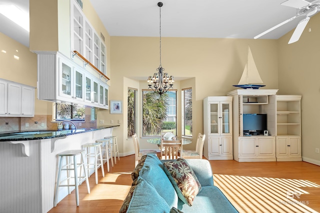 living room with light hardwood / wood-style floors, ceiling fan with notable chandelier, and a towering ceiling