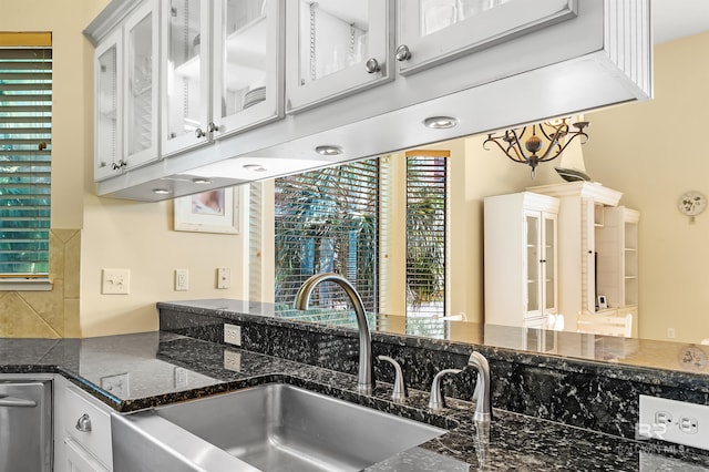 kitchen featuring dark stone counters, a wealth of natural light, sink, and white cabinetry