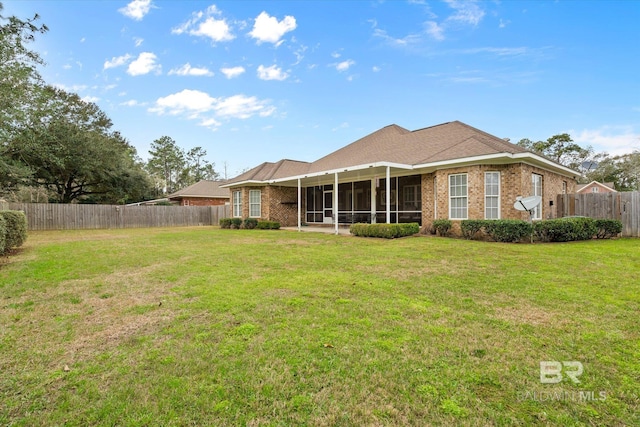 back of property featuring brick siding, a fenced backyard, a yard, and a sunroom