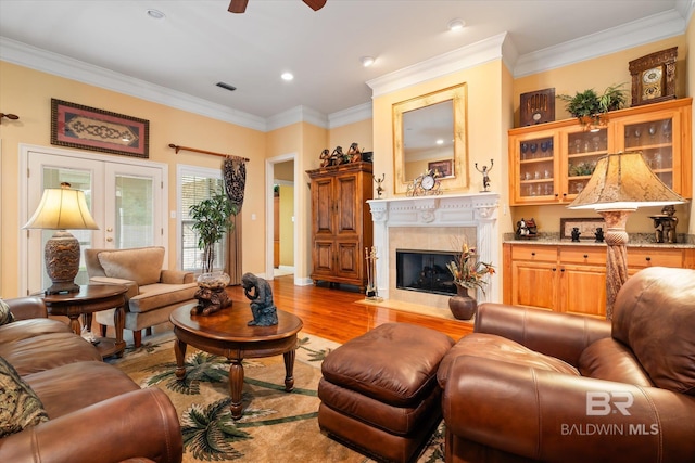 living room with a fireplace, light wood-style flooring, french doors, and ornamental molding