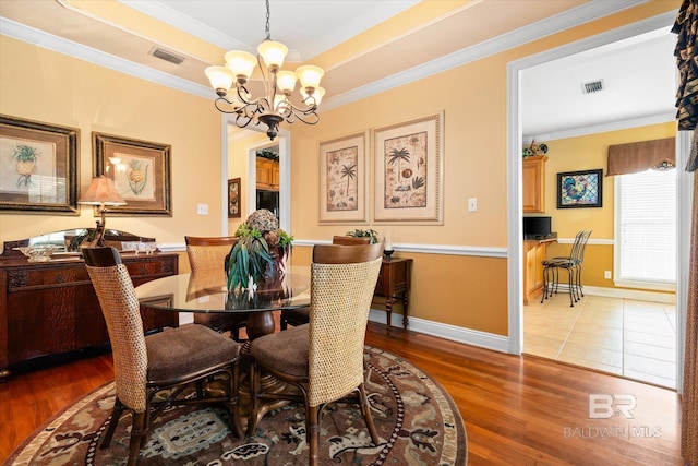 dining space featuring wood finished floors, visible vents, an inviting chandelier, a tray ceiling, and ornamental molding