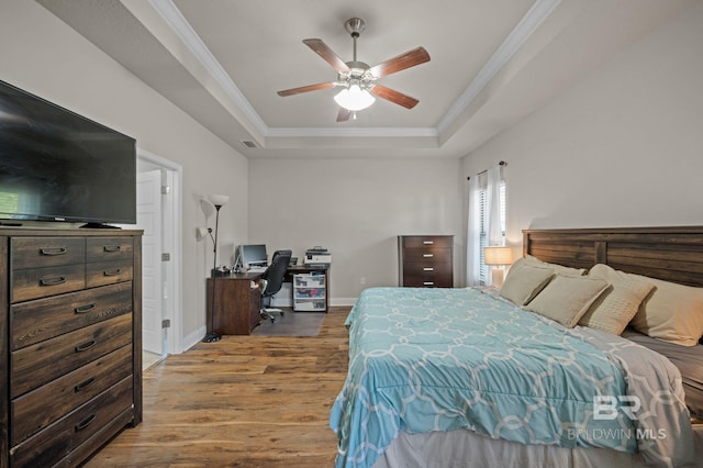 bedroom with visible vents, wood finished floors, baseboards, ornamental molding, and a tray ceiling