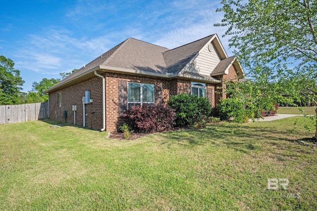 view of home's exterior with a lawn, brick siding, fence, and roof with shingles
