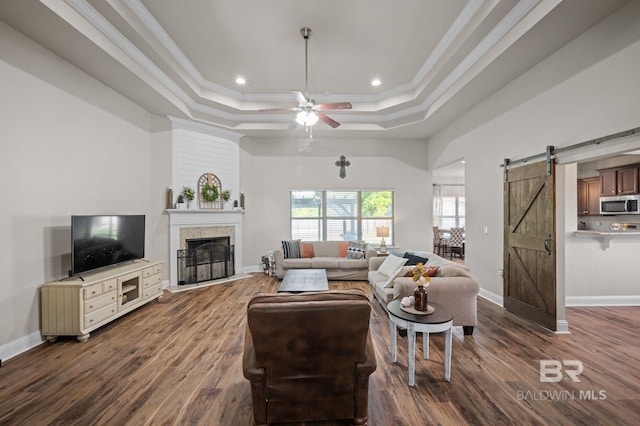 living area with crown molding, a tray ceiling, a barn door, and dark wood-type flooring