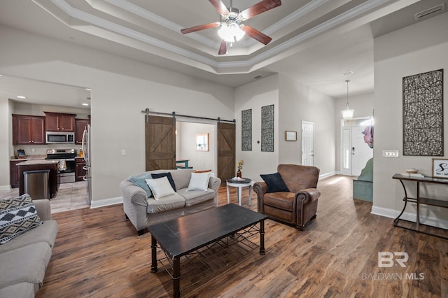 living area with wood finished floors, a tray ceiling, a barn door, and visible vents