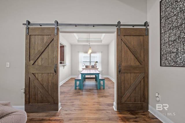 interior space featuring baseboards, a tray ceiling, a barn door, and wood finished floors
