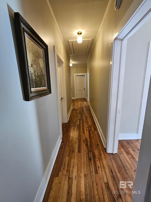 corridor featuring attic access, dark wood-type flooring, crown molding, and baseboards