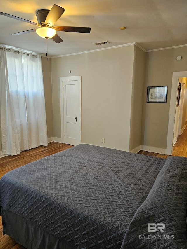 bedroom featuring baseboards, visible vents, ceiling fan, wood finished floors, and crown molding