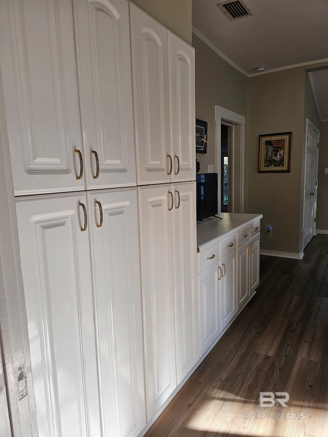 hallway featuring dark wood-style flooring, visible vents, crown molding, and baseboards