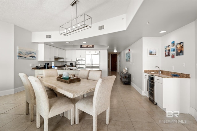 dining space with a textured ceiling, light tile patterned floors, sink, and beverage cooler