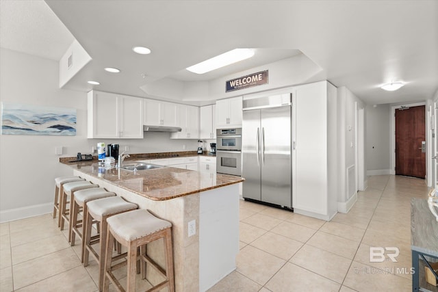 kitchen with dark stone counters, kitchen peninsula, light tile patterned floors, appliances with stainless steel finishes, and white cabinetry