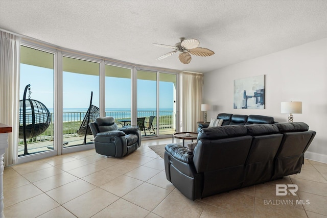 living room featuring a textured ceiling, ceiling fan, light tile patterned floors, a water view, and a wall of windows