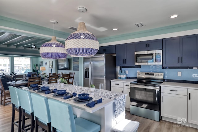 kitchen with pendant lighting, white cabinetry, appliances with stainless steel finishes, and light hardwood / wood-style floors