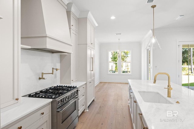 kitchen featuring custom exhaust hood, stainless steel range, sink, pendant lighting, and white cabinets