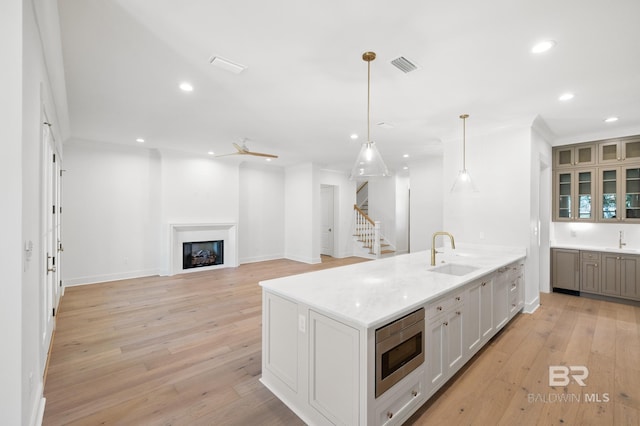 kitchen featuring stainless steel microwave, sink, ceiling fan, an island with sink, and decorative light fixtures