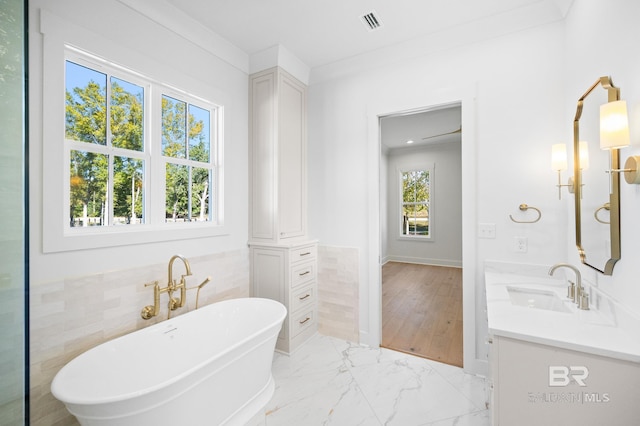 bathroom with a bathing tub, vanity, ornamental molding, and tile walls