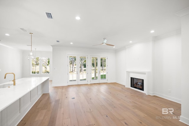 unfurnished living room featuring ceiling fan, sink, crown molding, and light hardwood / wood-style floors