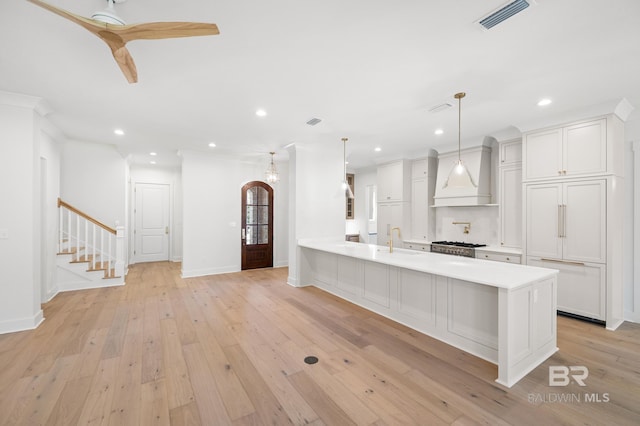 kitchen with premium range hood, white cabinetry, sink, and decorative light fixtures