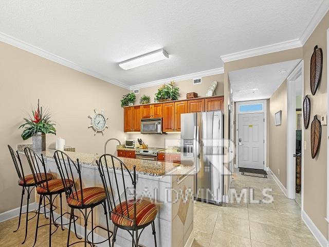 kitchen with a kitchen breakfast bar, stainless steel appliances, ornamental molding, and light stone counters