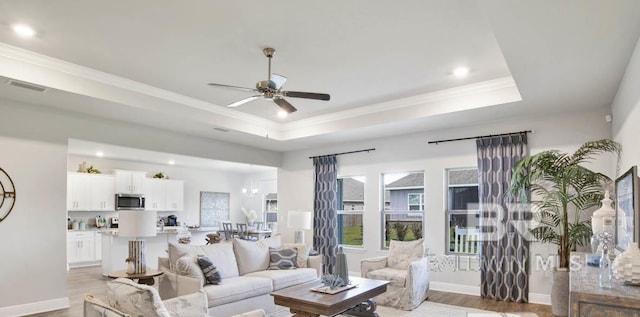 living room featuring wood-type flooring, a raised ceiling, ceiling fan, and crown molding