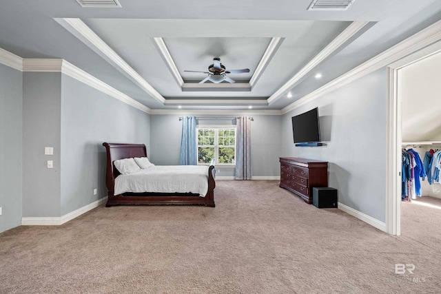 bedroom with light carpet, a walk in closet, a tray ceiling, ceiling fan, and crown molding