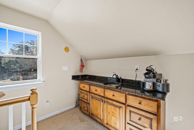 kitchen with dark stone counters, light colored carpet, lofted ceiling, and sink