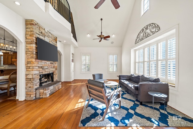 living room featuring hardwood / wood-style floors, ceiling fan, a fireplace, and a high ceiling