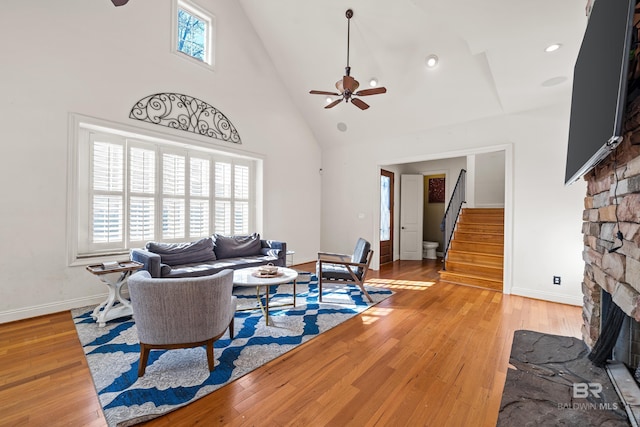 living room featuring ceiling fan, a fireplace, high vaulted ceiling, and light hardwood / wood-style flooring