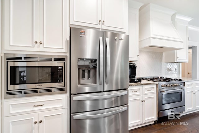 kitchen with stainless steel appliances, light stone counters, backsplash, white cabinets, and custom range hood