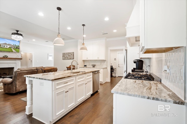 kitchen with light stone counters, a kitchen island with sink, sink, decorative light fixtures, and white cabinets